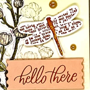 Close on the sentiment "hello there" below a stamped dragonfly on a greeting card.