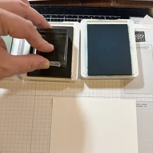 A hand presses an acrylic block onto an ink pad.