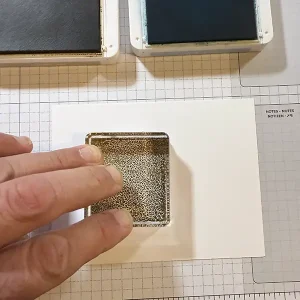 A hand presses an acrylic block with ink on it onto a piece of white card stock.