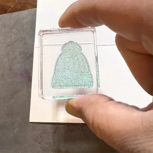 A stamp of a beanie is held between someone's fingers.